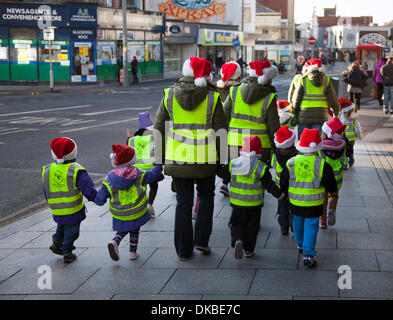 K ids Walking Across Street in Blackpool, Lancashire, Großbritannien 4.. Dezember 2013. Rückansicht der Risikoeinschätzung Kinder und Lehrer im Vorschulalter, geschützt mit weihnachtsmützen und gut sichtbarer Kleidung, auf dem Weg zum Tag der offenen Tür des Winter Gardens Blackpool Opera House Theatre. Eine Gelegenheit, alle Bereiche kostenlos zu besuchen, etwas, das noch nie zuvor in den Winter Gardens getan wurde, um das Jahr 135 mit der lokalen Gemeinde und den Besuchern von Blackpool zu feiern. Stockfoto