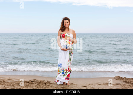 Schwangere Frau stehen am Strand, die Hände auf Bauch Stockfoto