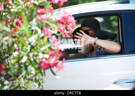 Reife Frau, Auto zu fahren, trägt Verkleidung und Gesicht mit der Hand versteckt Stockfoto