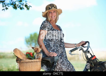 Reife Frau auf e-Bike mit Hund und Gemüse im Korb Stockfoto