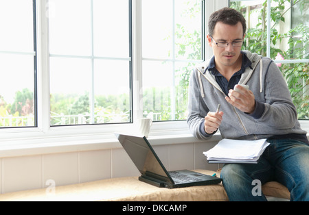 Mitte erwachsener Mann mit Handy in Fensterplatz sitzen Stockfoto