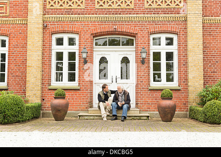 Vater und Sohn sitzen vor Haustür Stockfoto