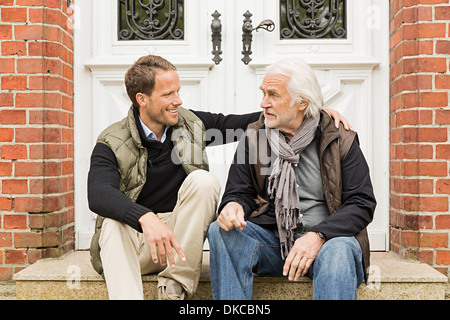 Vater und Sohn sitzen vor Haustür Stockfoto