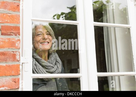 Ältere Frau, die durch Fenster Stockfoto