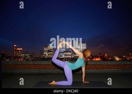 Mitte Erwachsene Frau praktizieren Yoga auf Stadt-Dach bei Nacht Stockfoto