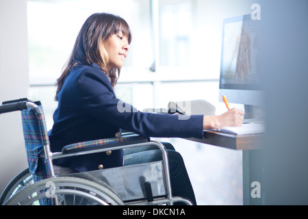 Frau im Rollstuhl, die Schreiben von Notizen Stockfoto