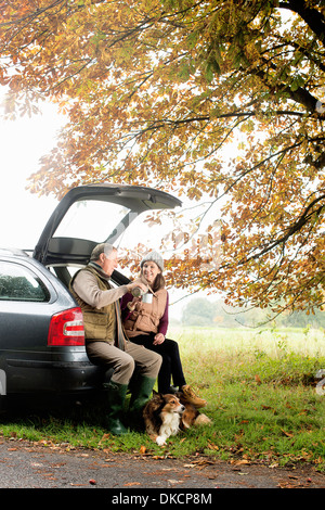 Älteres Paar mit Hunden teilen Kaffee aus Kofferraum, Norfolk, Großbritannien Stockfoto