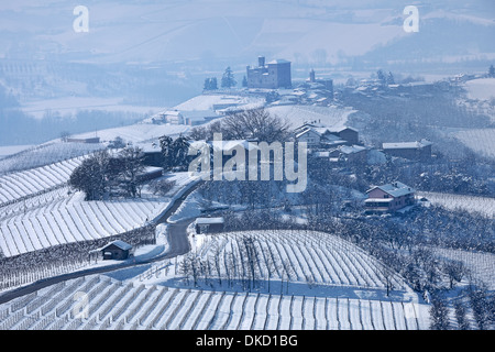 Schmale Straße durch Hügel bedeckt mit Schnee in Richtung kleines Dorf im Piemont, Norditalien. Stockfoto