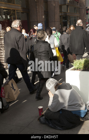 Obdachloser sitzt auf Bürgersteig demütig um Spenden während zu bitten Die Weihnachtseinkaufszeit auf der 5th Ave in NYC Stockfoto