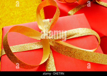 einige Geschenke verpackt, mit rotem Geschenkpapier und mit einem goldenen Band auf goldenem Hintergrund Stockfoto