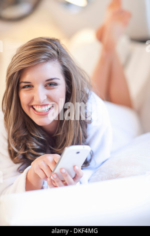 Porträt der jungen Frau auf Bett liegend mit Handy Stockfoto