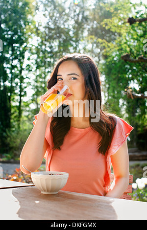 Porträt der jungen Frau trinkt Orangensaft im Garten Stockfoto