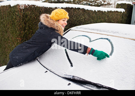 Frau Zeichnung Herzform auf Schnee bedeckt Windschutzscheibe Stockfoto