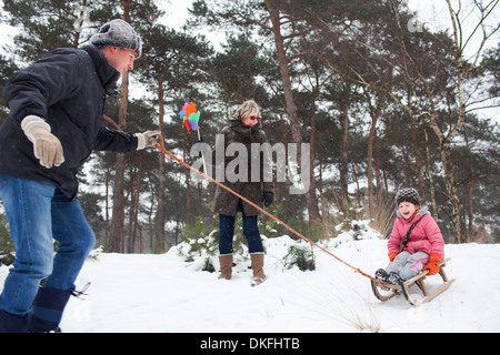 Vater und Großmutter ziehen Mädchen am Schlitten im Schnee Stockfoto