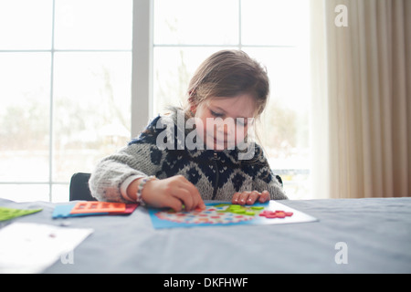Junges Mädchen saß am Tisch, die Konzentration auf Spiel Stockfoto