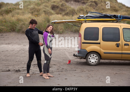 Mann hilft Frau anziehen Neoprenanzug am Strand Stockfoto