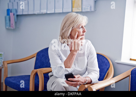 Ältere Patientin mit Handy im Krankenhaus Wartezimmer Stockfoto