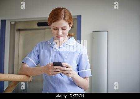 Krankenschwester, Blick auf Handy vor Krankenhaus Aufzug Stockfoto