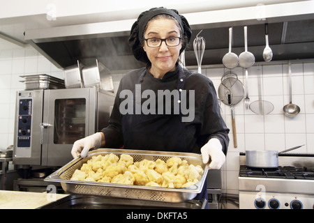 Frau in Restaurantküche, arbeiten mit Tablett mit Blumenkohl Stockfoto