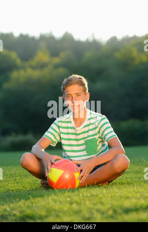 Teeange Junge sitzt mit Fußball auf der Wiese, Oberpfalz, Bayern, Deutschland, Europa Stockfoto