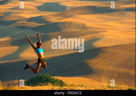 Junge weibliche Läufer springen vor Freude in den Feldern, Bainbridge Island, Washington State, USA Stockfoto