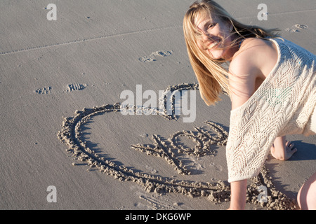 Lächelnde Frau schreiben Liebesbotschaft im Sand, Breezy Point, Queens, New York, USA Stockfoto