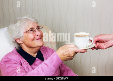 Gebrechliche süße, glückliche alte ältere Frau, die einem Betreuer während des täglichen Help-Home-Besuchs eine Tasse Tee überreicht und lächelt. England GB Stockfoto