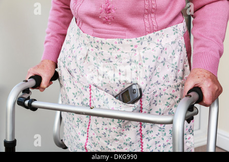 Ältere ältere Frau, die ein schnurloses Telefon Hörer in eine Schürze Tasche mit einem Walker für Unterstützung stehen. England, Großbritannien, Großbritannien Stockfoto