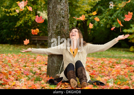 Glückliche junge Frau sitzt unter einem Baum im Herbst Stockfoto