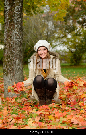 Lächelnde junge Frau an einem Baum im Herbst Stockfoto