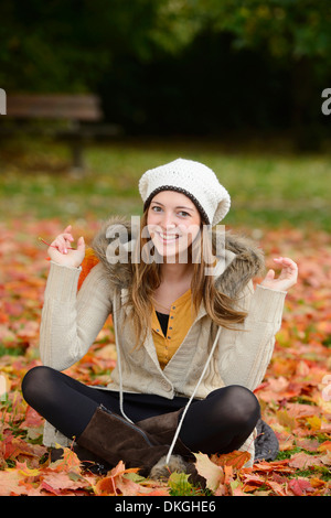 Lächelnde junge Frau sitzt im Herbst Blätter Stockfoto