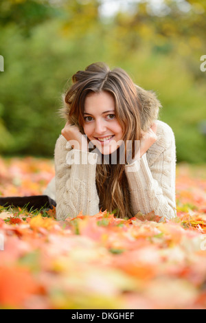 Lächelnde junge Frau liegend im Herbst Blätter Stockfoto