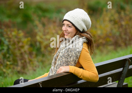 Lächelnde junge Frau sitzen auf einer Bank im Herbst Stockfoto
