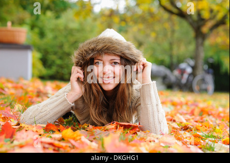 Lächelnde junge Frau liegend im Herbst Blätter Stockfoto