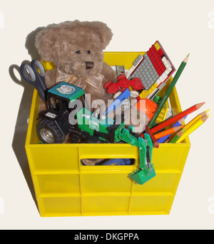 Gelber Kunststoff Kiste - gefüllt mit Kinderspielzeug wie Teddybär, Lego, Traktor, Buntstifte - auf weißem Hintergrund Stockfoto