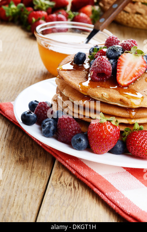 Weißen Teller voll mit Pfannkuchen mit Erdbeeren Himbeeren Heidelbeeren und Honig Stockfoto