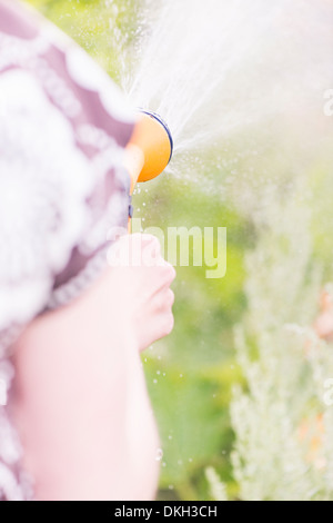 Rückansicht der Frau hält einen Garten Sprinkler, Bewässerung von Pflanzen hautnah Stockfoto
