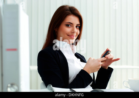 Junge glücklich Geschäftsfrau hält Smartphone im Büro Stockfoto