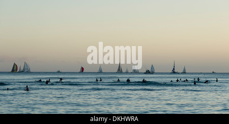 Surfer und Segelboote im Meer bei Sonnenuntergang, Waikiki, Honolulu, Oahu, Hawaii, USA Stockfoto