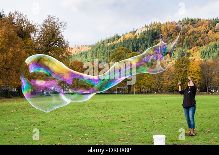 Eine Frau macht eine riesige Seifenblase mit Regenbogenfarben mit einer Blase Wand in Betws-y-Coed, Conwy, North Wales, UK, Großbritannien Stockfoto