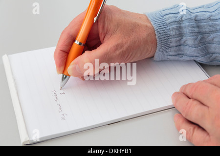 Ein rechtshändiges Senior Frau schreiben einen persönlichen Brief an einen Freund mit einem Pad Papier auf einer Tischplatte. England Großbritannien Stockfoto