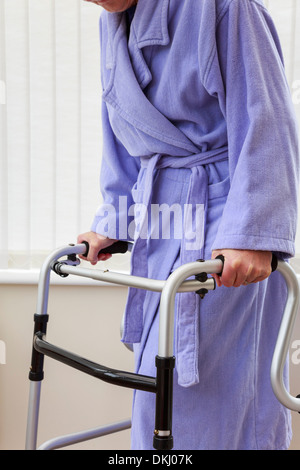 Ältere ältere Frau im lila Bademantel Holding mit einer Gehhilfe Walker oder Support Trolley für den Gang in ein Heim. England Großbritannien Großbritannien Stockfoto