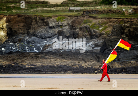 Bademeister trägt waring Fahnen an den Rand des Wassers in Cornwall Stockfoto