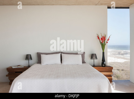 Vase mit Blumen neben Bett im Schlafzimmer mit Blick aufs Meer Stockfoto