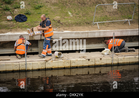 Drei Arbeiter arbeiten Männer bei der Arbeit tragen orange hi-Vis Westen, Inspektion oder Wartung eine konkrete Ufermauer. Stockfoto