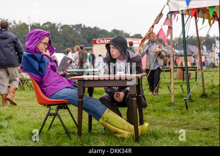 Ein paar saß an einem Tisch im Freien auf einem Musikfestival. Die junge Frau liest. Stockfoto