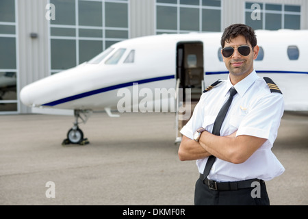 Pilot mit verschränkten Armen vor Privatjet Stockfoto