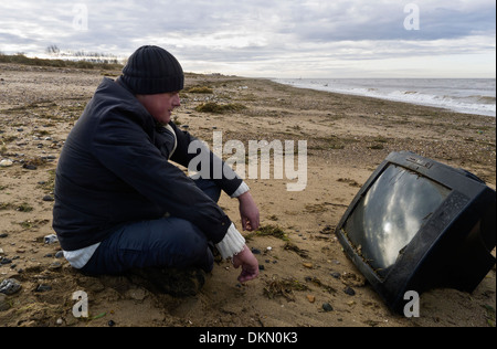 Mann beobachtet einen Fernseher an einen Strand gespült. Stockfoto