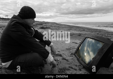 Mann beobachtet einen Fernseher an einen Strand gespült. Stockfoto