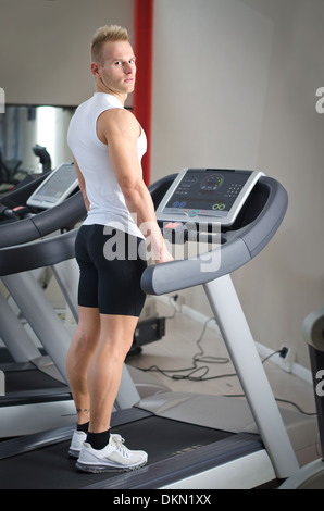 Blonde attraktive junge Mann auf Laufband, gesehen von hinten, Blick in die Kamera Stockfoto